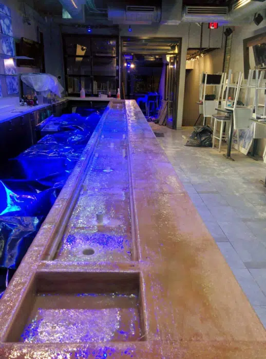 Long resin-coated commercial bar top with an integral drainage trough, lit blue