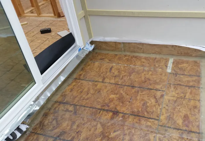 Exterior balcony deck of resin-coated OSB meeting a sliding door threshold and flashed siding wall