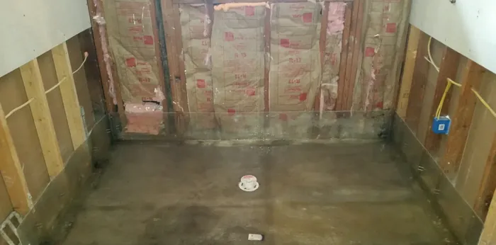 Rectangular grey shower pan sloped to a capped drain with membrane turned up the surrounding walls