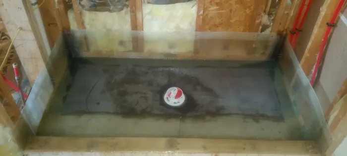 Rectangular shower pan coated dark grey, membrane turned up walls to a level line, capped drain