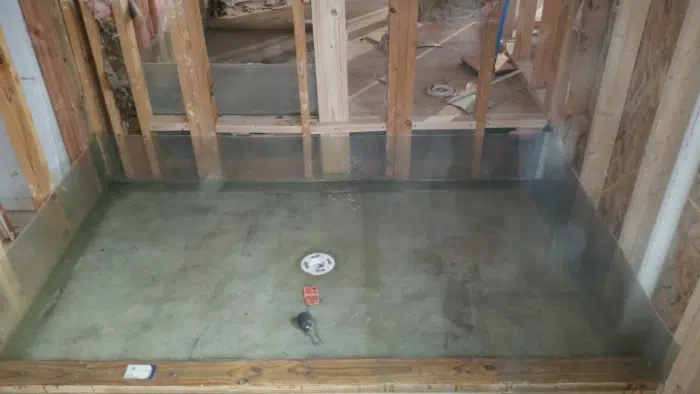 Wide shower pan sealed with waterproofing membrane, continuous upturn where the floor meets the walls, capped centre drain