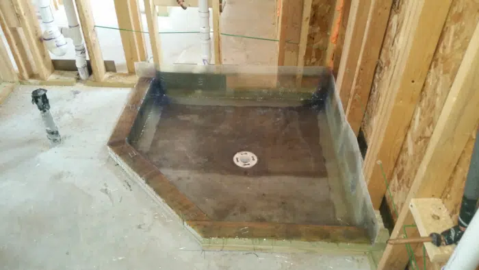 Angled-corner shower pan waterproofed over curb and floor, drain flange set in sloped basin