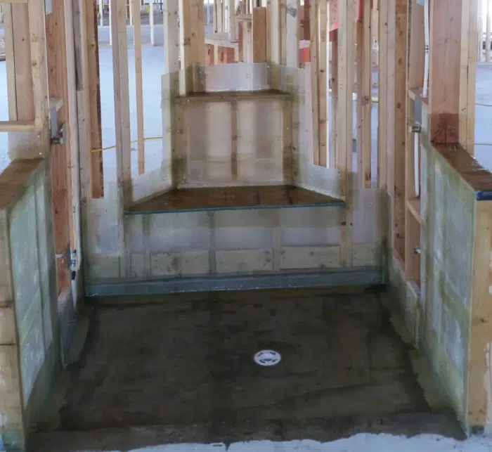 Head-on shower under construction, pale resin membrane over pan, curb, bench and stepped alcove, drain centered